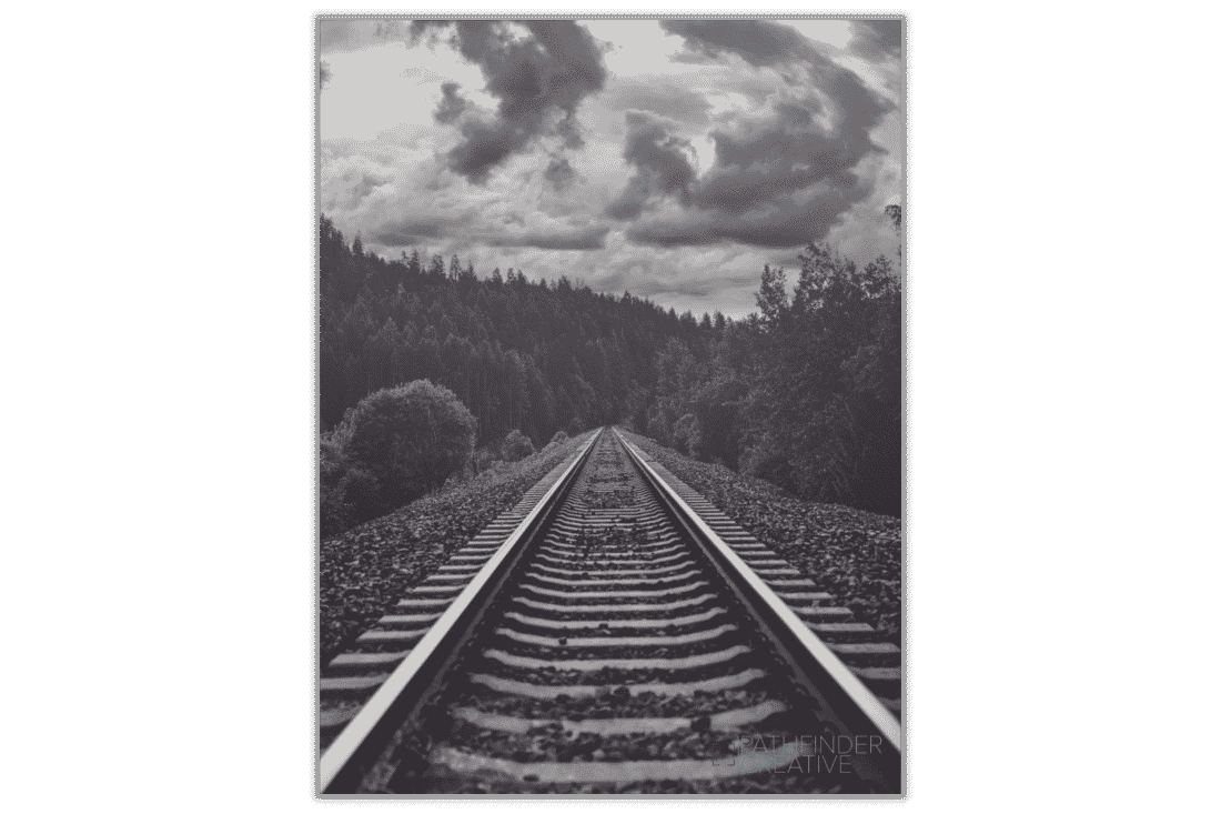 black and white photo of railroad tracks and forest with storm clouds