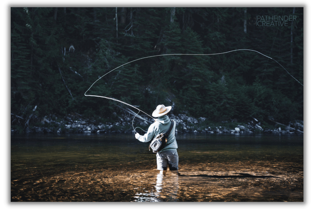 man fly fishing in deep green river with forest