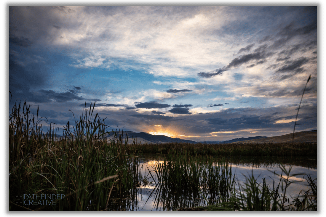 colorful sunrise over march with cat tails, blue skies, orange sunrise, and white clouds